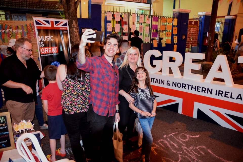 Three people smile to a selfie in front of the GREAT Britain and Northern Ireland sign.