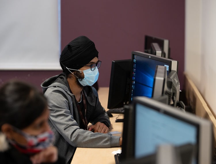 Image of student wearing a mask on a computer in the classroom
