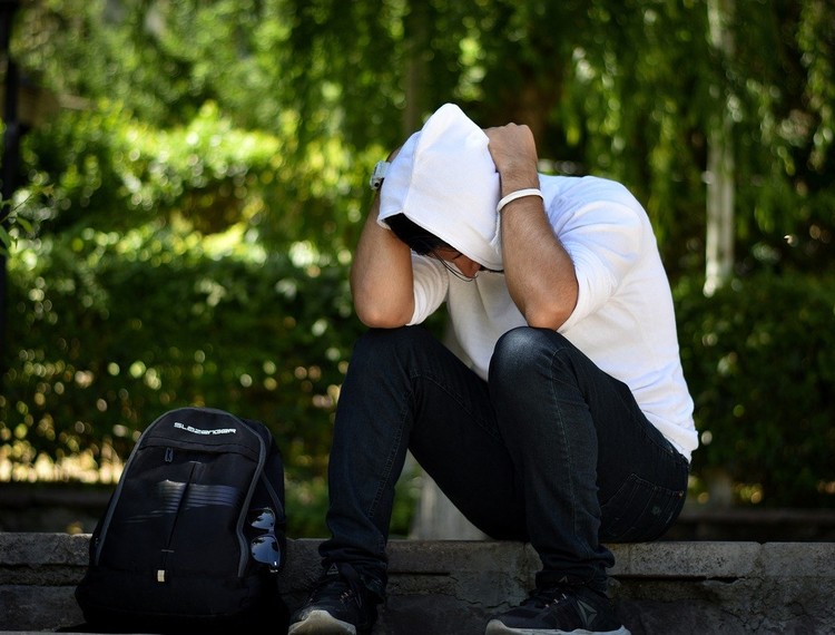 Student with head in their arms, sitting on a kerb