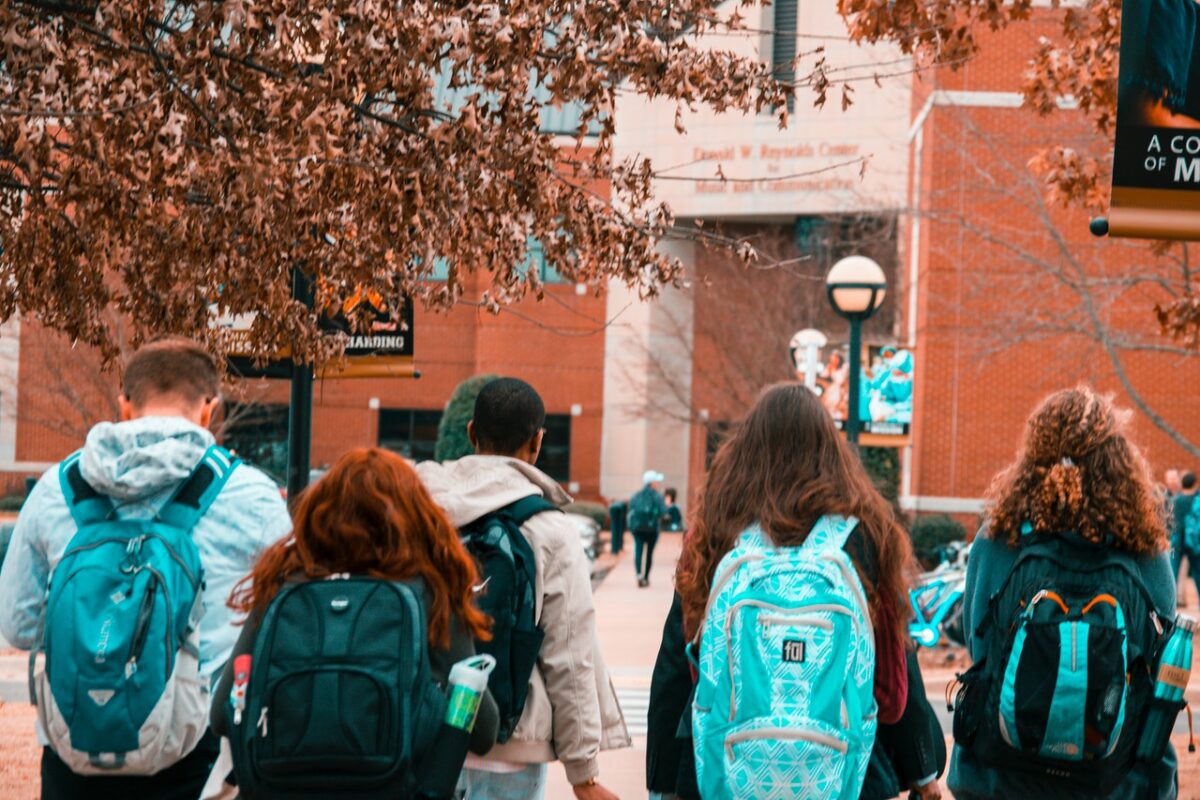 Students walking away from camera towards school with backpacks on