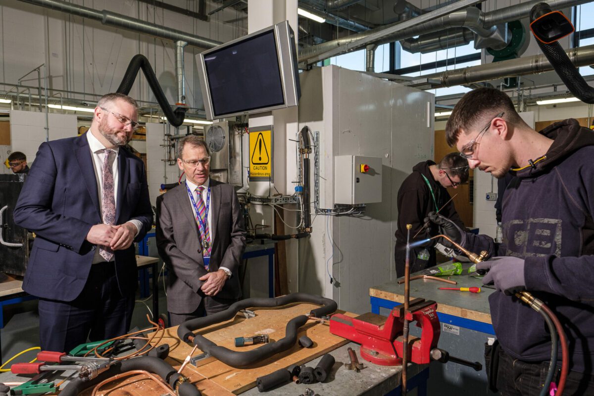 Andrew Stephenson MP and Derek Whitehead, the CEO & Principal of Leeds College of Building, stand to the left of a student demonstrating construction skills in a workshop at the College's South Bank Campus.