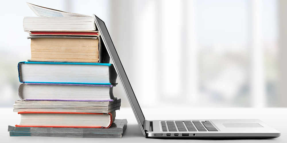 Image of a stack of books next to an open laptop