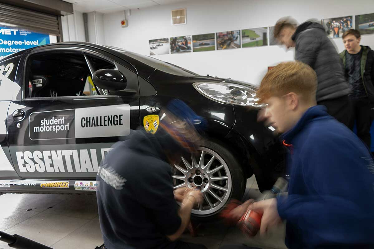 Two students are removing a wheel from the race car. They are moving fast, and blur through the image.