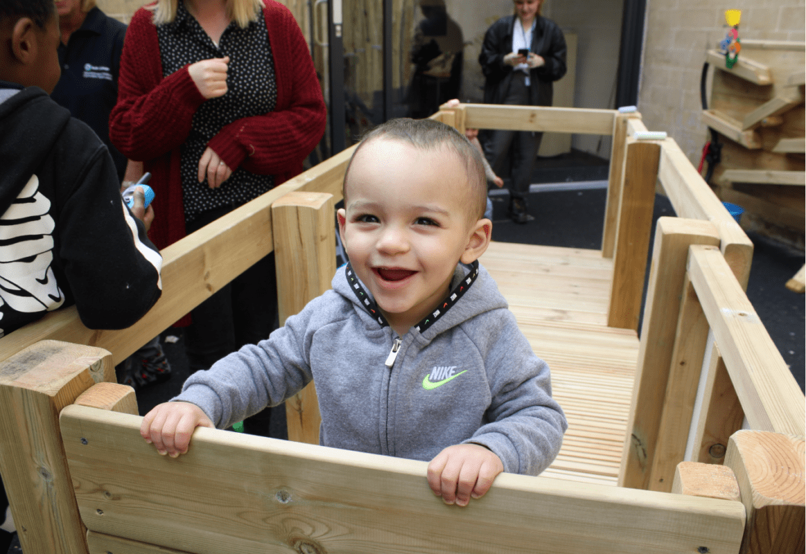 Young child smiling on outdoor climbing frame at Bath College Creche