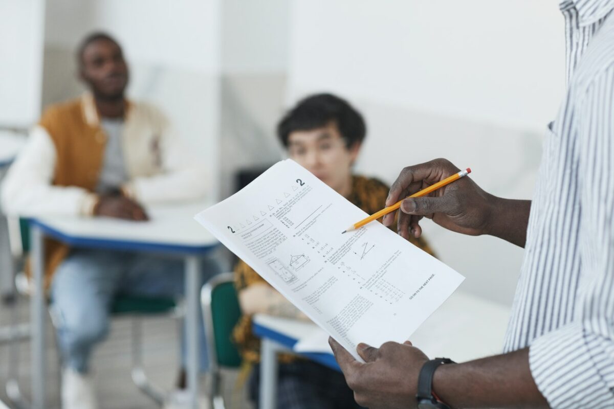 someone holding an exam paper with students sat at desks in the background