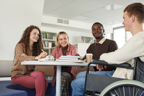 4 students at a table, one in wheelchair, looking at each other smiling