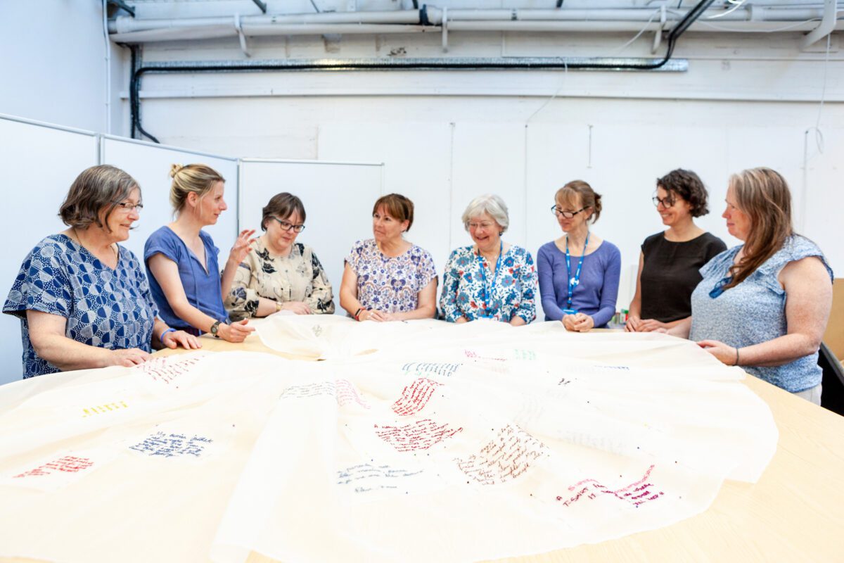 Artist Hannah Lamb (the second to the left ) sat at a table with Bradford College students working on the ‘Fragments of a Dress’ embroidery project.