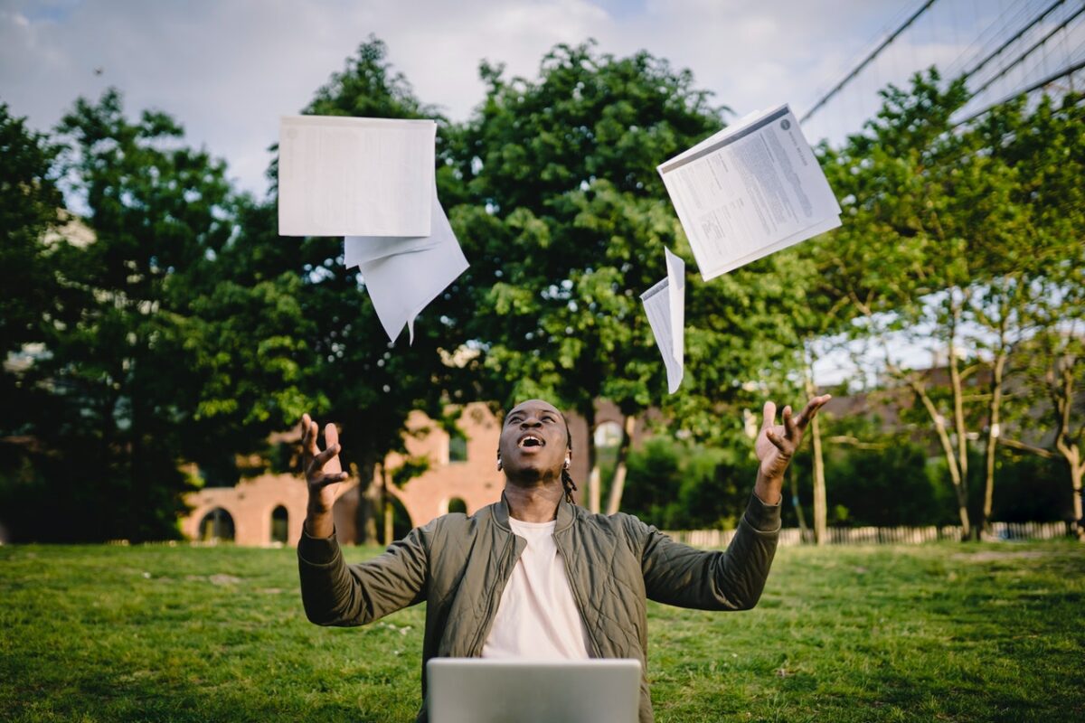 Student with laptop throwing paper in air