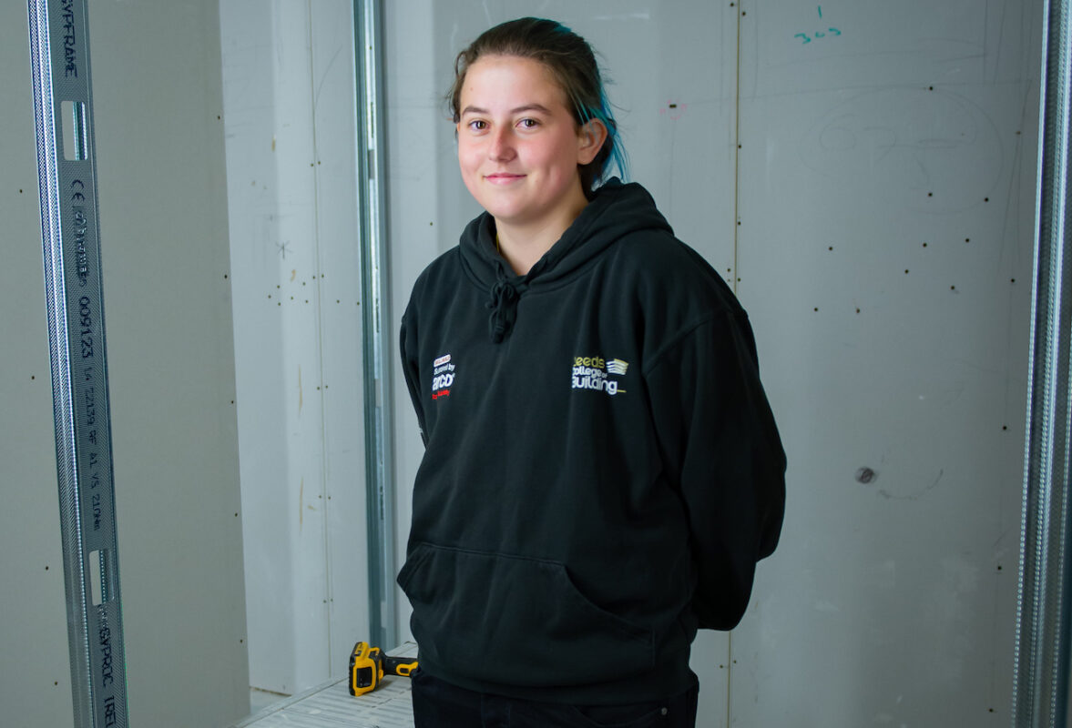 Leeds College of Building apprentice, Zara Dupont, stands in front of a Drywall she is constructing.