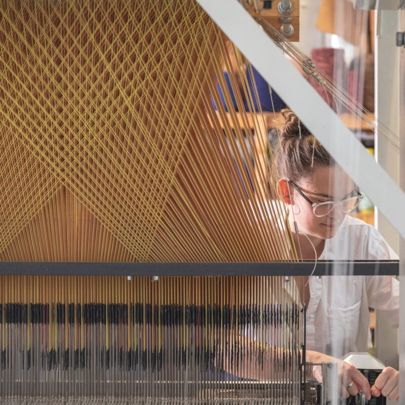 Bradford College lecturer and weaver Hannah Robson sits at a large industrial loom.