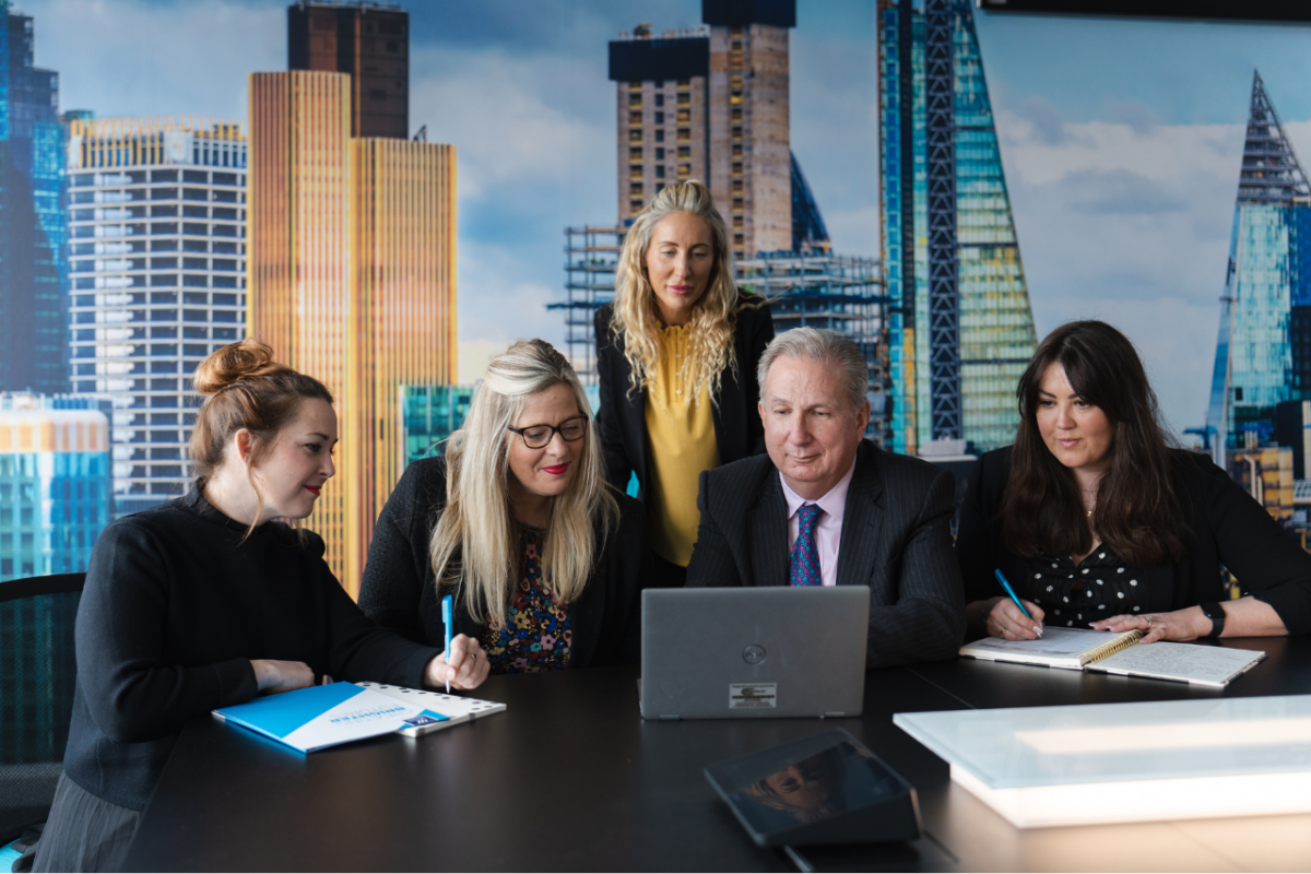 Nicola Lace, Zoe Bodely, Sam Mayhew, Leila Morne and Sir Paul Philips looking at laptop in boardroom