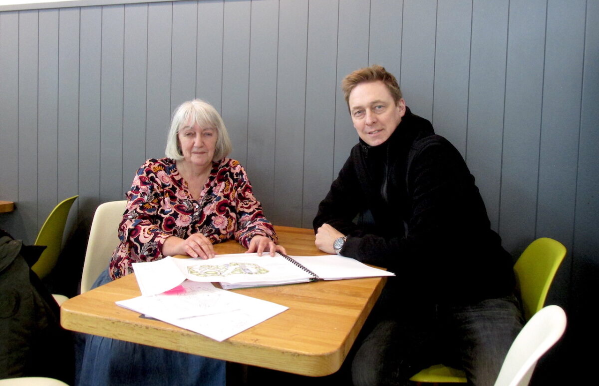 Garden designer Carolyn Hardern sits at a wooden table next to landscaper Jon Jarvis with garden design plans in front of them.