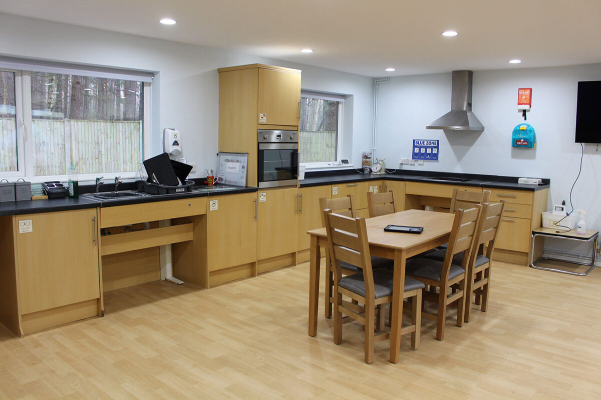 A large kitchen/dining area with kitchen cabinets around the outside and a table with chairs in the middle.