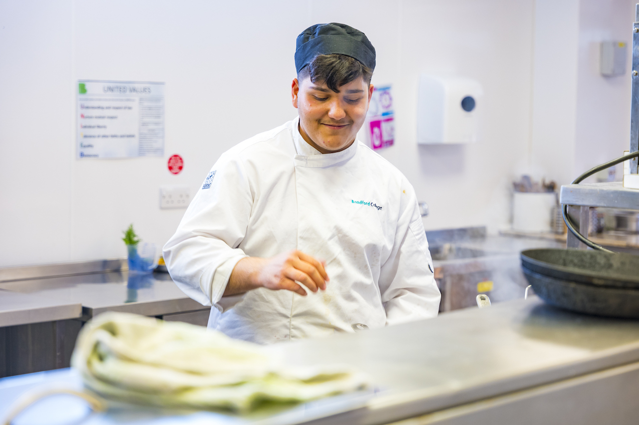 A Bradford College catering student wearing chef's whites prepares a dish in the college kitchen.