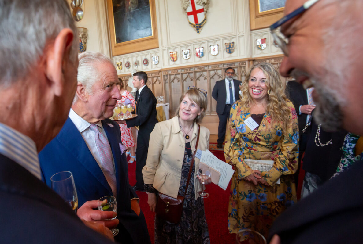 King Charles III meets guests at a drinks reception in a great hall at Windsor Castle. Bradford College ESOL lecturer, Esther Wilkey, stands two to his right and is laughing as the King address the group.