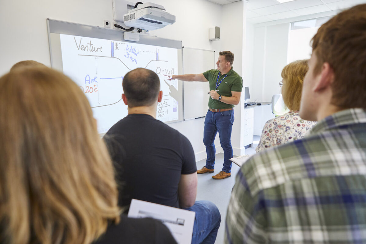 A higher education lecturer stands at front of a whiteboard and teaches a class.