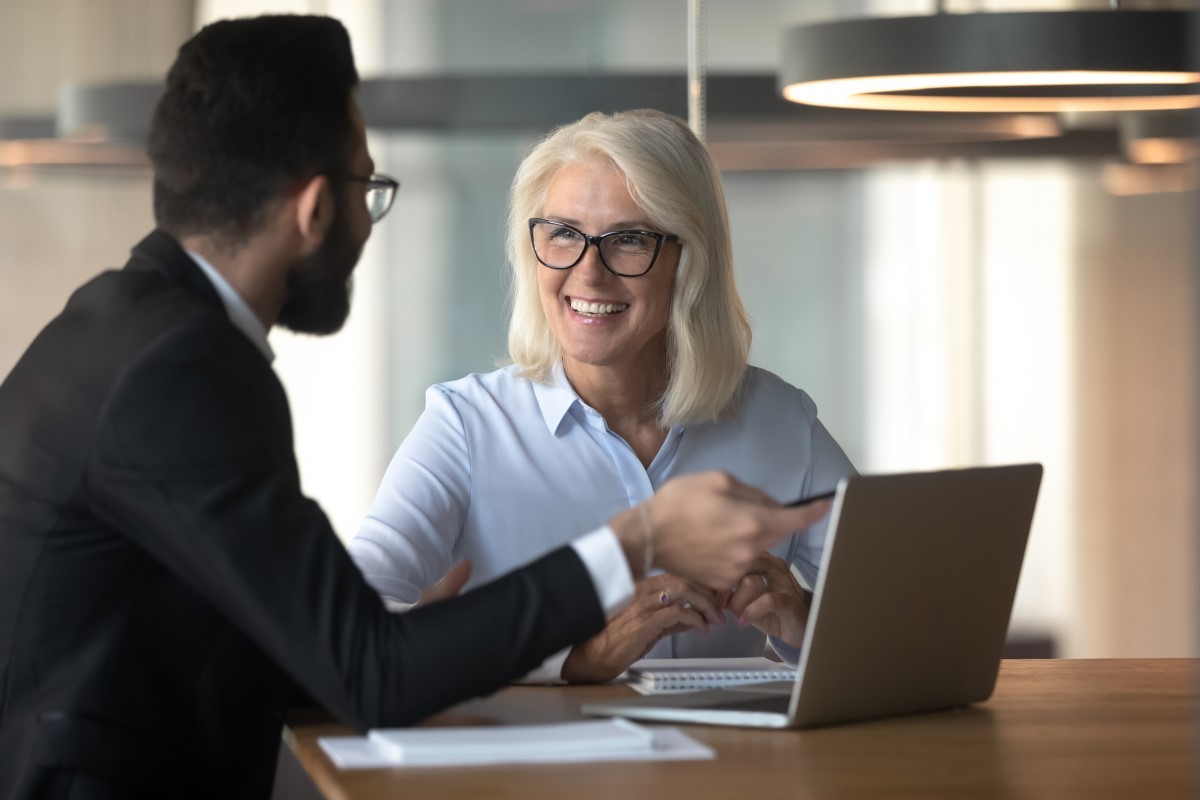 A woman and a man have a discussion in front of a laptop in an office setting.