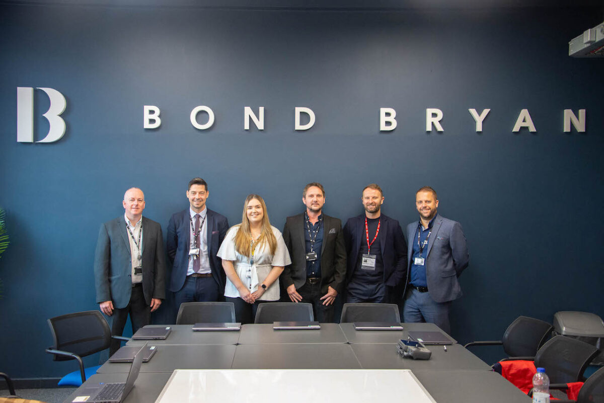 Bond Bryan CEO Matt Hutton stands with Bradford College staff in the new Bond Bryan Academy base room at Trinity Green Campus in front of Bond Bryan wall signage.