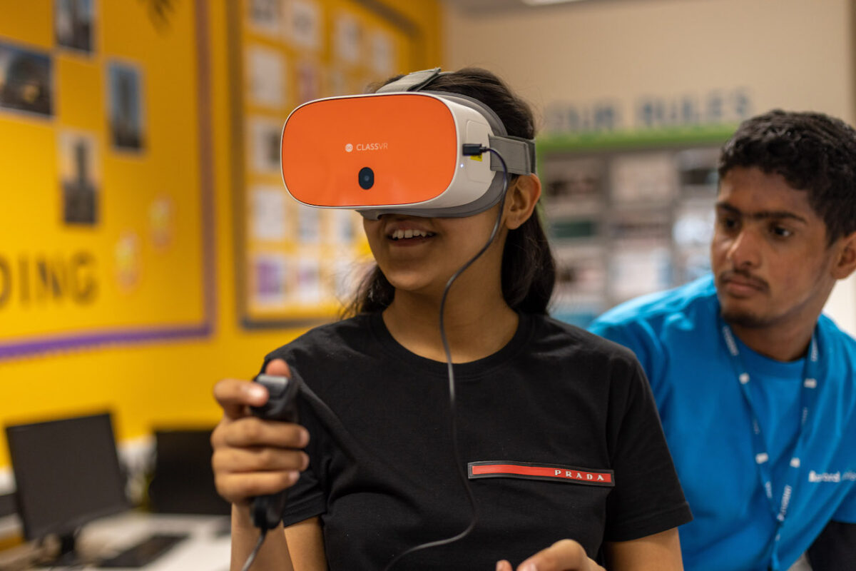 A female school pupil in a classroom wearing VR goggles.