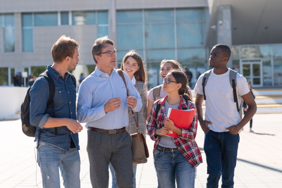 Teacher talking to a group of students outdoors at the university â education concepts