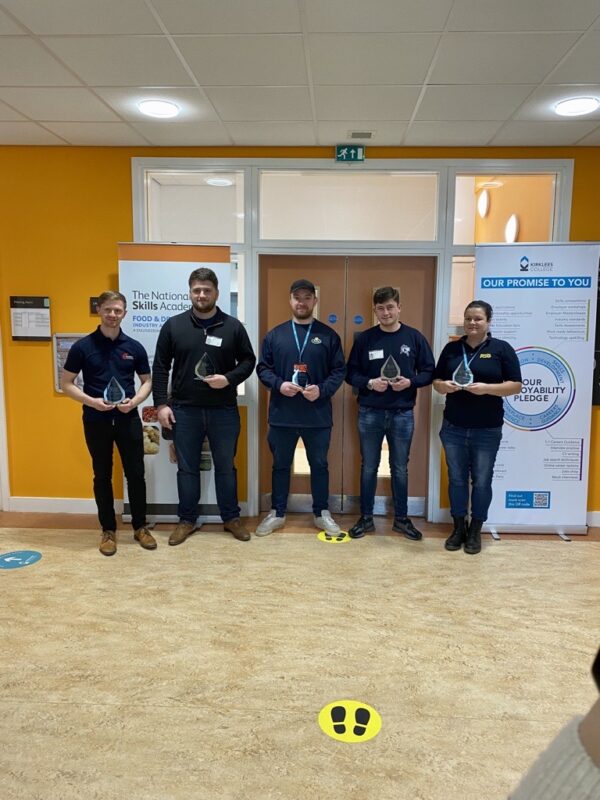 Food and Drink Apprentice award winners hold their trophies standing in a line outside two double doors and a banner stand