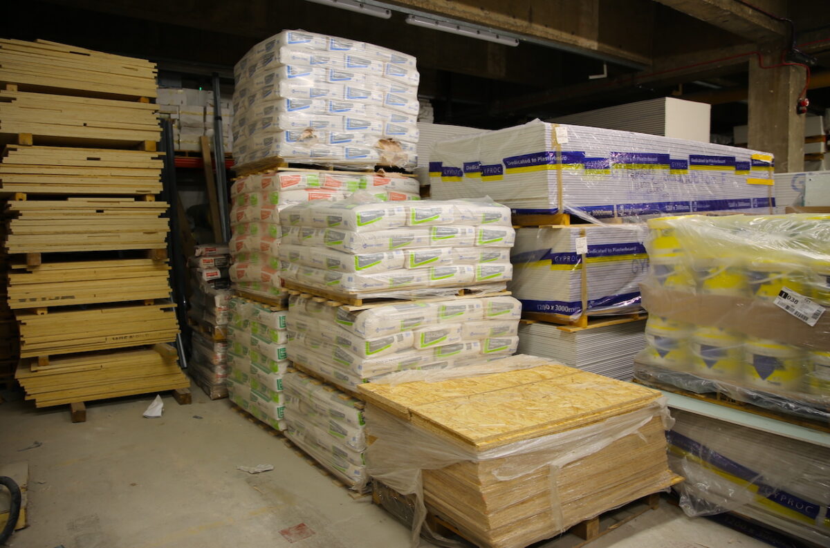 A storage room filled with tall piles of plaster bags and pallets of building materials.