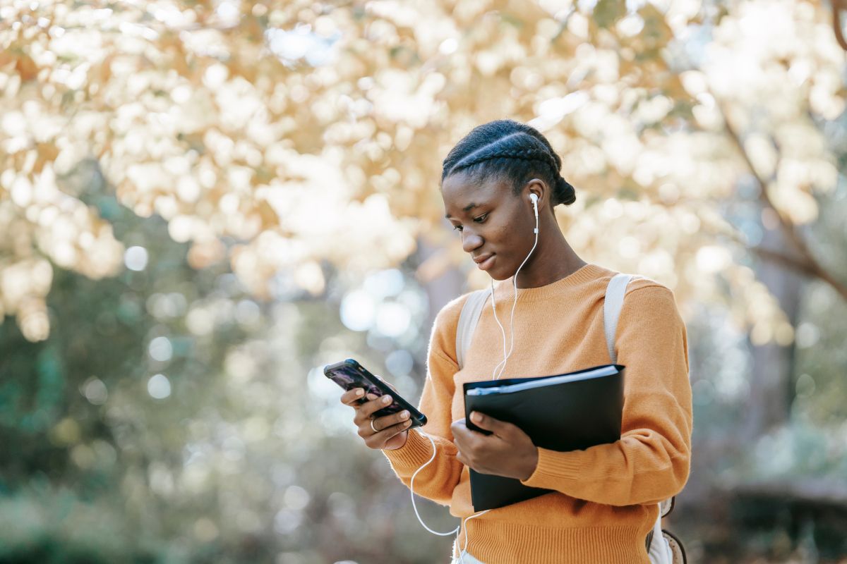 student holding books and looking at phone