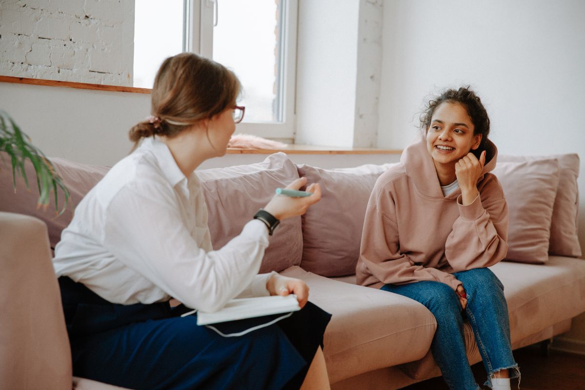 2 girls talking while sat on a sofa