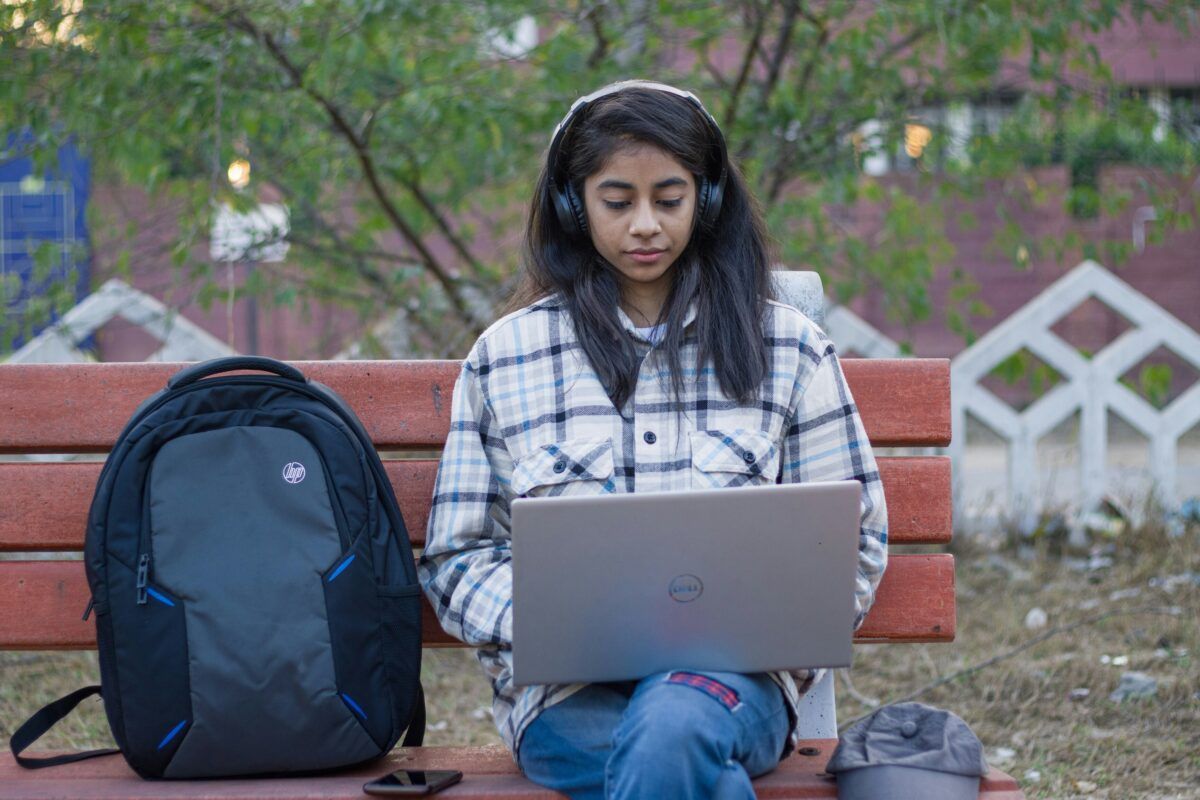 lady sat on a bench wearing headphones while using a laptop
