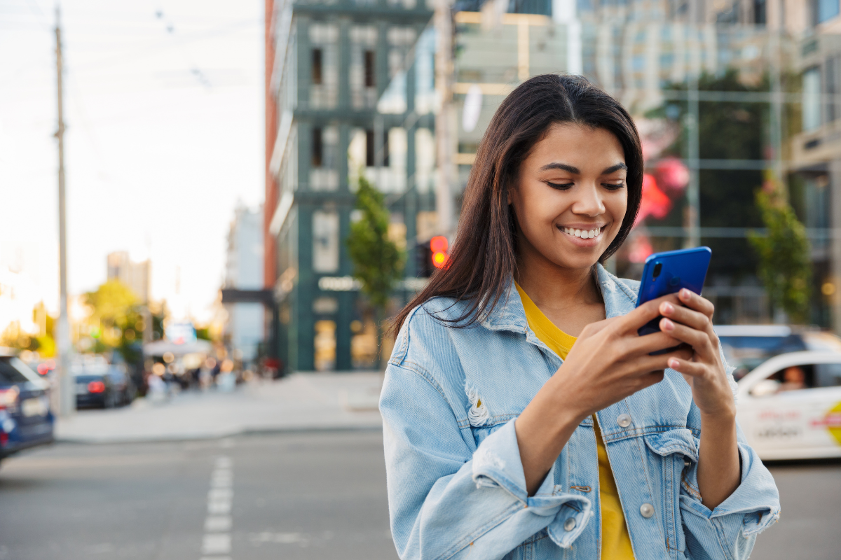 Young woman smiling while looking at her phone in the street