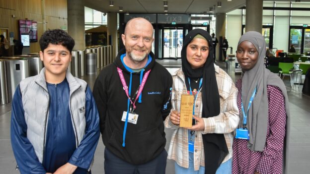 Bradford College ESOL students stand either side of their tutor holding the Planet Earth Games trophy.