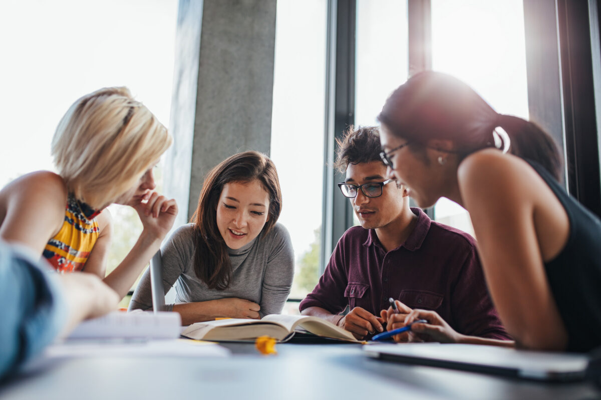 Group of young people sitting at table reading books