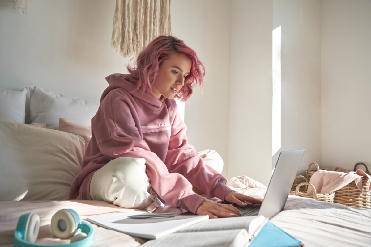 Young lady who looks like a student sitting on her bed working on a laptop