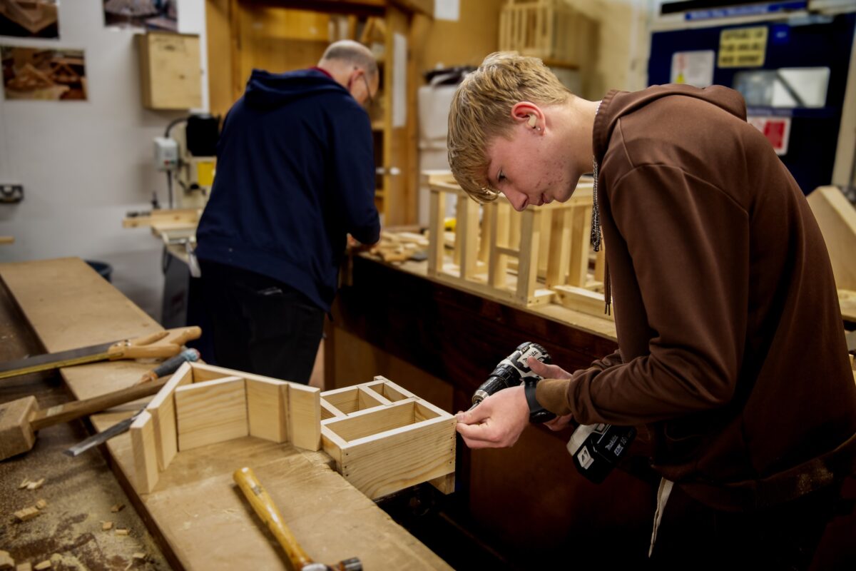 An LCB student uses and electric screwdriver to attach wooden pieces of a bug hotel together in a joinery workshop.