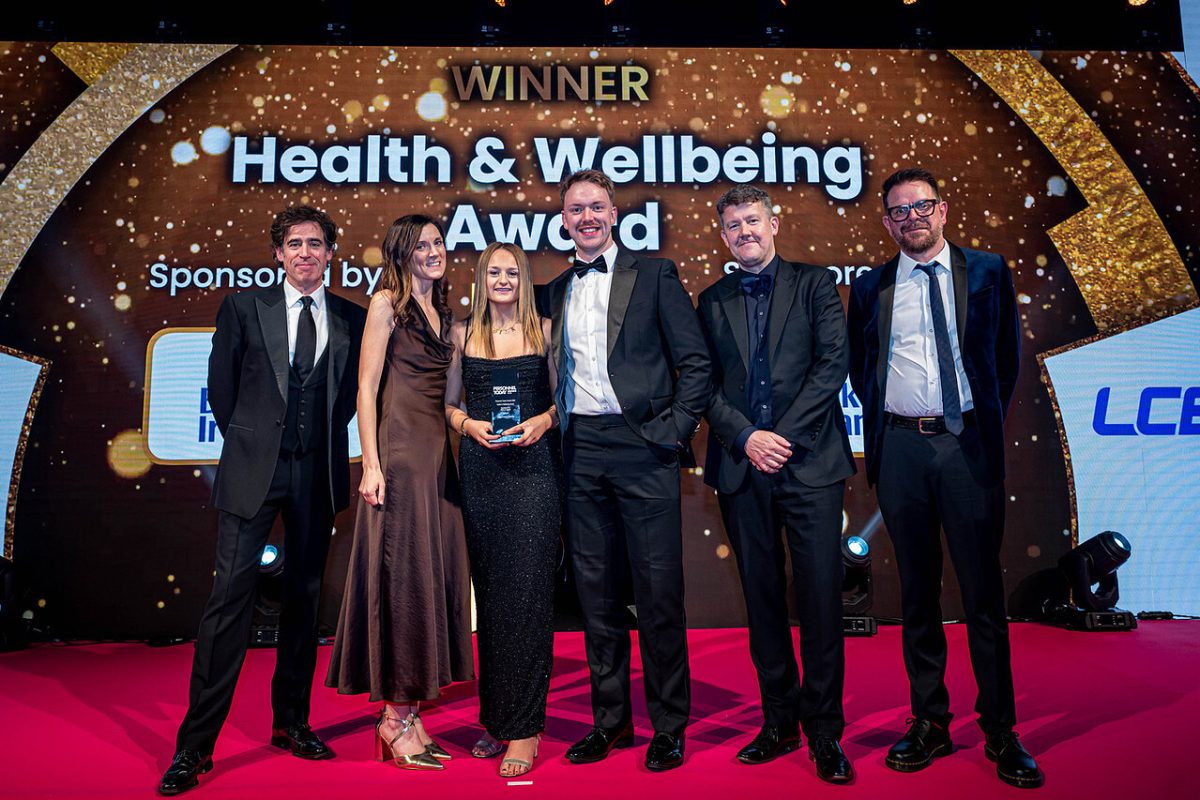 LCB staff stand on stage dressed in black-tie attire and pose with the ‘Health & Wellbeing’ trophy at the Personnel Today Awards 2025. To their left is host and comedian/actor Stephen Mangan.