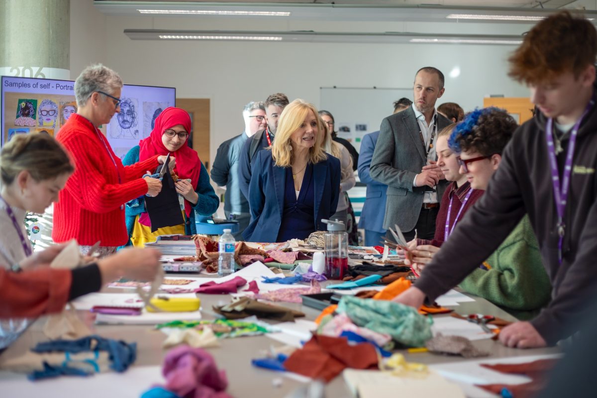 Tracy Brabin, Mayor of West Yorkshire, stands at the end of a long table covered in craft materials. Bradford College students stand on either side of the table making craft items as the Mayor watches, with other guests standing behind her in the background.