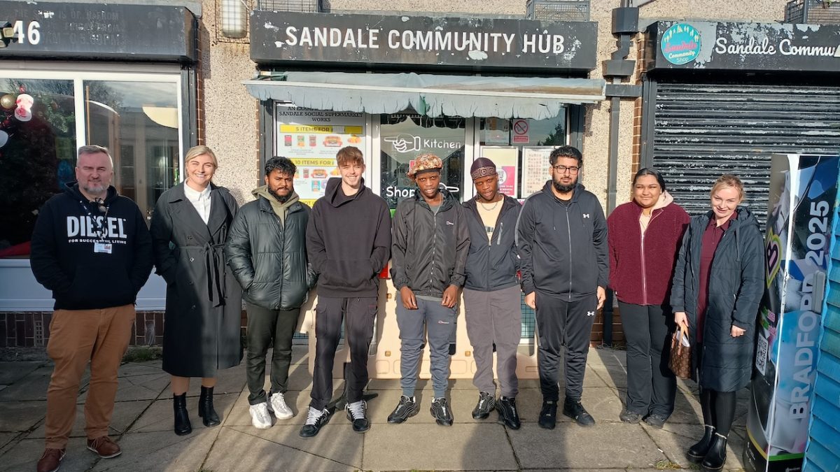 A group of young people stand outside the Sandale Trust building ready to start their training. Their supervisor, John Wells, stands to the left of the picture.