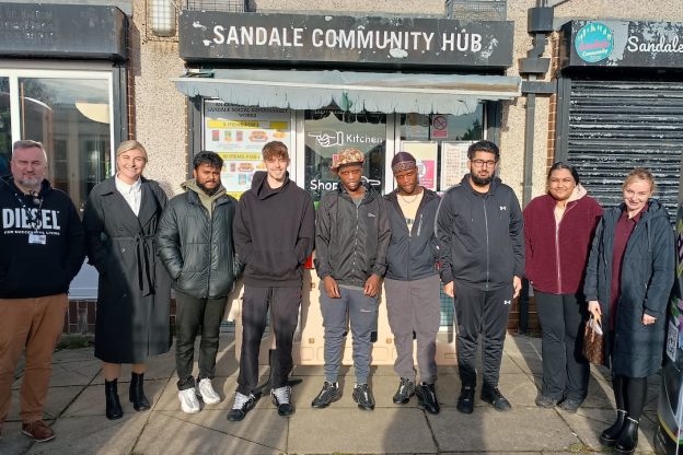 A group of young people stand outside the Sandale Trust building ready to start their training. Their supervisor, John Wells, stands to the left of the picture.