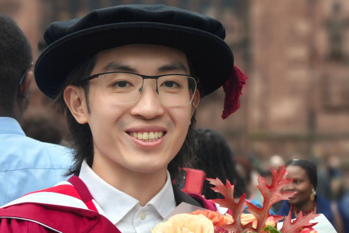 A head-and-shoulders photo of a man in a graduate cap, and glasses, smiling at the camera.