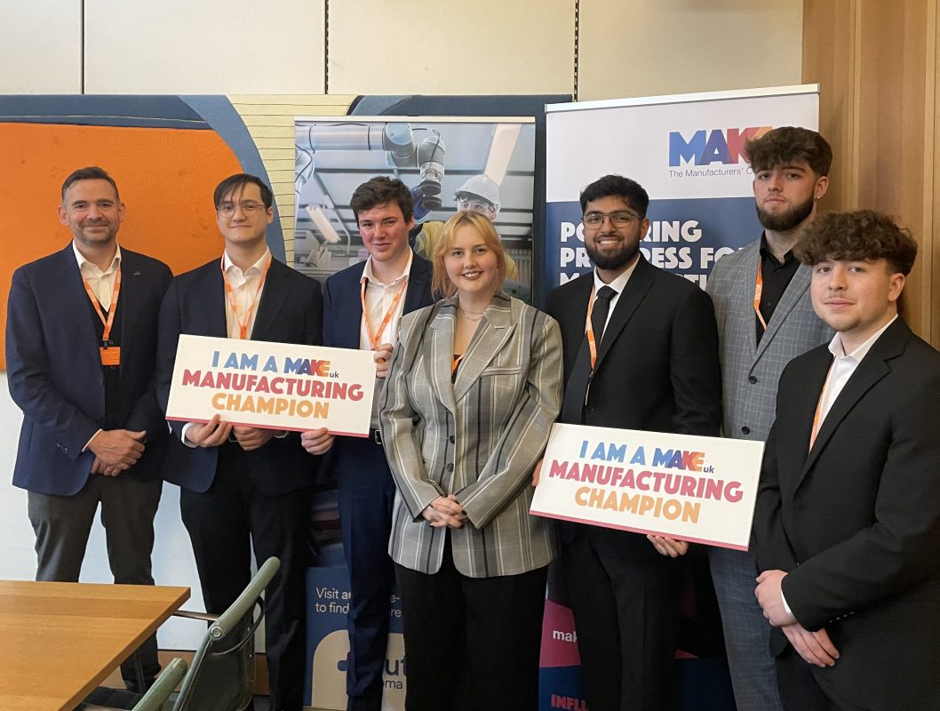 A group of five male apprentices and their two colleagues from Automate BEST pose as with manufacturing champions signs during a drop-in session in UK Parliament