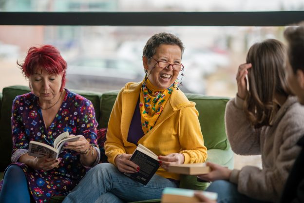 Three women sat on a green couch reading and smiling