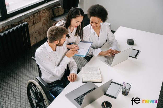 Man in a wheel chair working with colleagues, looking like they are analysising figures at work. Latest Labour Market Figures Show Disabled People Are Twice As Likely To Be Unemployed Than Non-disabled People