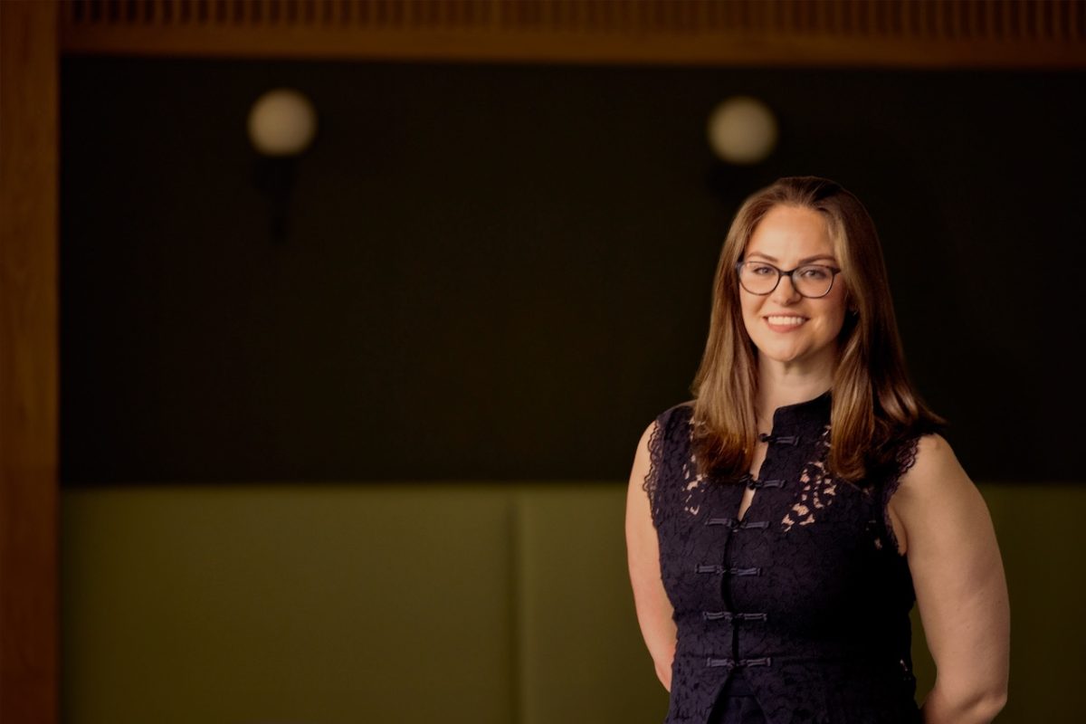 Carly Sidebottom, Leeds College of Building Assistant Principal -Partnerships & Adults, poses against a black background. She has long brown hair, glasses, and is wearing a sleeveless navy top.