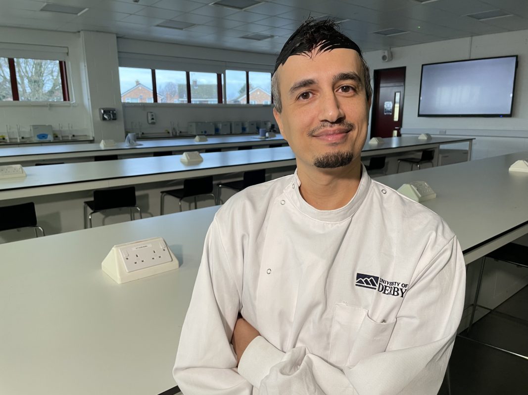 A man in a white lab coat smiles at the camera