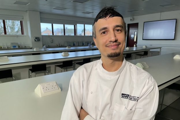 A man in a white lab coat smiles at the camera