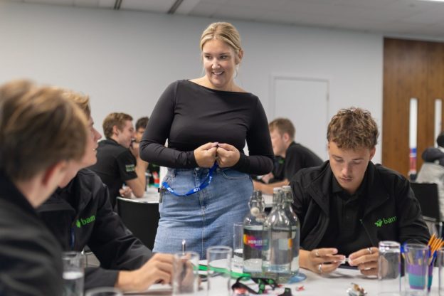 A female teacher stands next to a table of male apprentices.