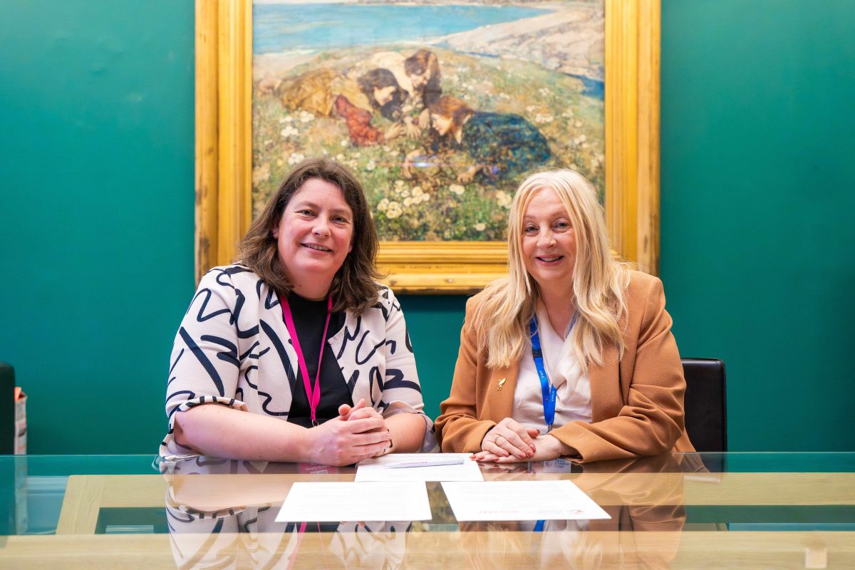 Two women sitting at a desk in front of a big painting