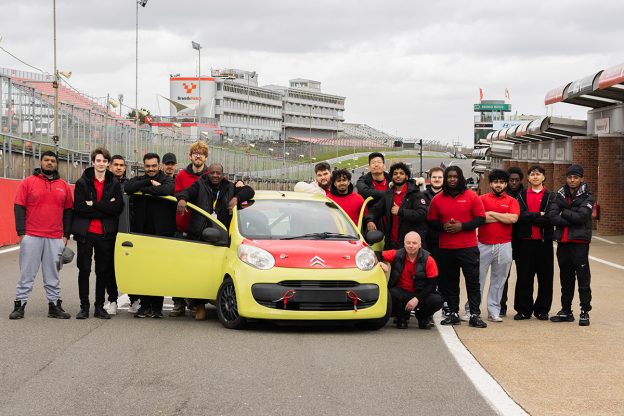 students stand around green race car on the brands hatch pit stop