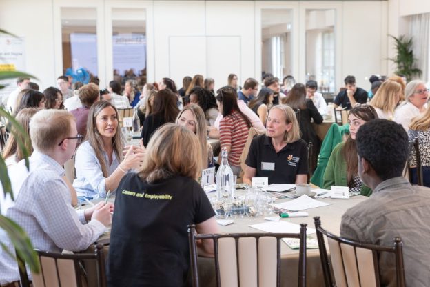 A packed room of people in discussions sat at round tables.