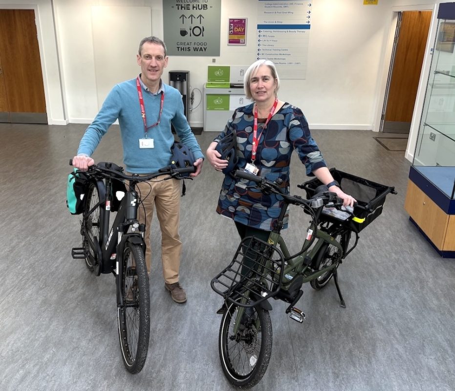 Two people standing at Borders College reception alongside two e-bikes